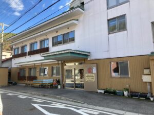 介護施設の玄関・車寄せ。茶色い外壁パネルと白い建物が特徴